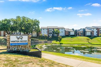 A sign for Water Ridge sits in front of a pond and houses.